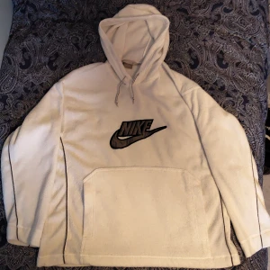 Vit Nike fleece hoodie - Vit Nike fleece hoodie köpt second hand. Storlek M och sparsamt använd, inga fläckar eller andra brister, skick 10/10. Nike logga på ena axel och detaljer på sidor och insidan av armarna. Säljs pga fel storlek. Skriv om du har några frågor :) 