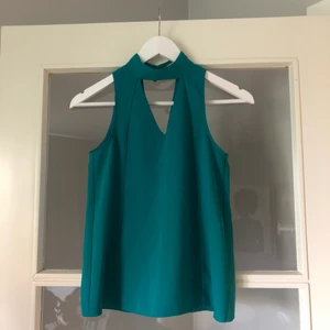 Topp med utskärning - Turkos topp med utskärningar. Knäpps baktill med guldfärgade knappar. 