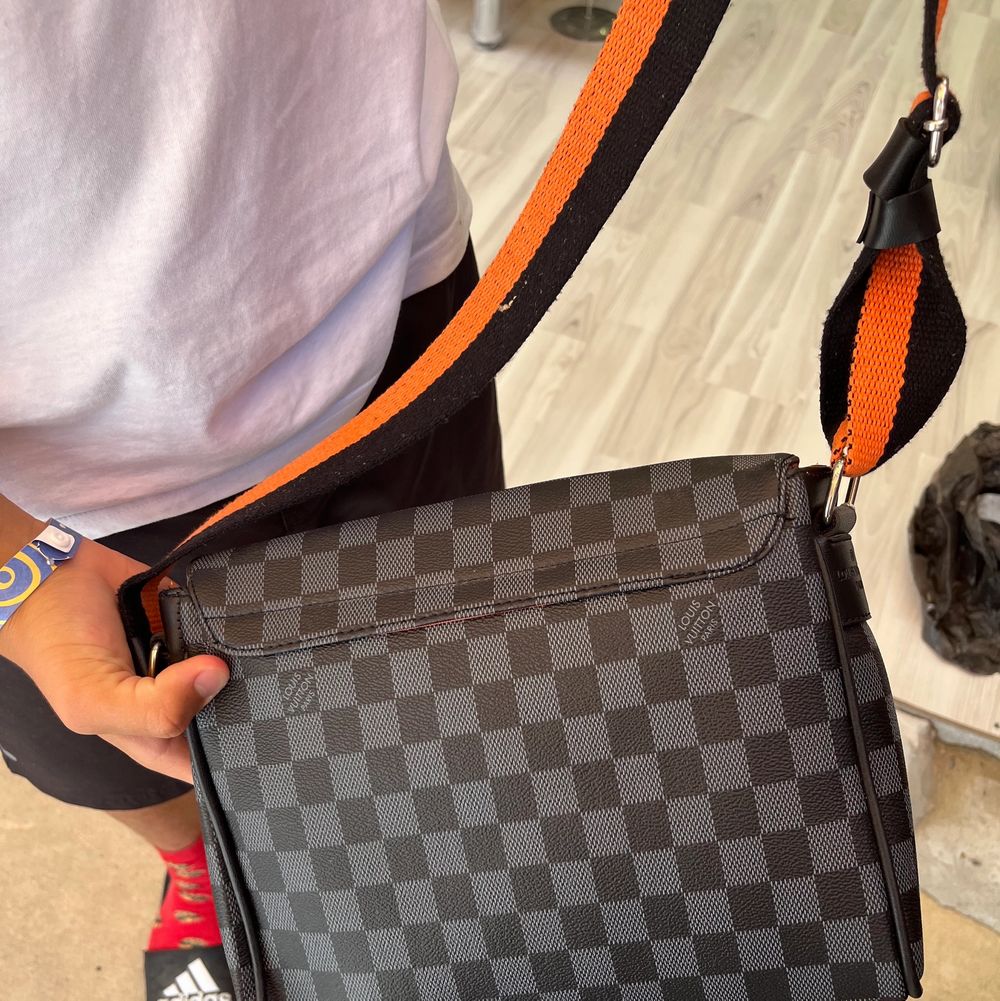 En A kopia av Louis Vuittons eftertraktade axelväska. Denna är svart och orange färgad. Remmen är justerbar, det finns 4 fack och den är oanvänd. . Väskor.