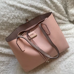 Rosa shoppingväska Guess - Stor väska från Guess, köpt för längesedan o glömts bort tyvärr varpå jag säljer, sparsamt använd. Kommer med en väska inuti som med fördel används separat. Måtten är ca 45 cm bredd och 30 cm i längd 