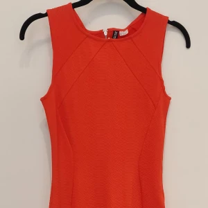Supersnygg tight klänning i korall från HM. - Supersnyggt sommarfodral. Stretchigt tyg, dragkedja bak. Adrig använd, prislapp kvar. Tyvärr för liten.  Kan skicka om intresse finns 