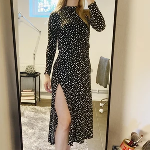 Prickig klänning med slitz - Otroligt smickrande och följsam klänning. Har en slits och ett band i midjan som går att knyta både bak, fram och i sidan. Svart med vita prickar. Enbart använd ett fåtal gånger. Storlek XS men stretchigt material, jag har vanligt vis S-M.