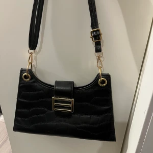 Svart väska  - Denna väska kommer ifrån SHEIN och har gulddetaljer, säljer denna för 60kr!