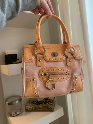 Orange guess väska  - Jättefin orange guess väska. Lite fläckar i då min ögonbrynspenna öppnades i väskan :( men det går säkert bort om man tvättar av de med något❤️använd ett fåtal gånger
