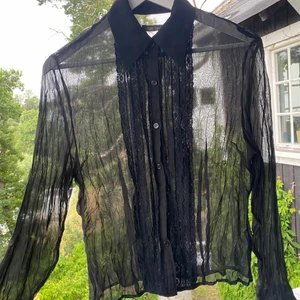 Transparent skjorta med spets - Transparent skjorta med spets längs knapparna i stl M  Det har tyvärr lossnat en knapp (se bild) men en kan ju lätt sy fast en ny :)  