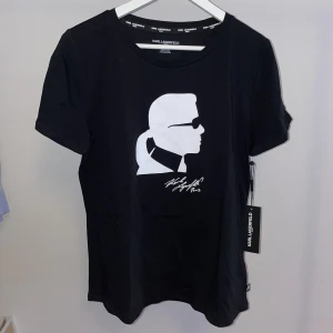 T-shirt med tryck, Karl Lagerfeld  - T-shirt med tryck från Karl Lagerfeld. Helt ny, oanvänd med lappar kvar. Funkar när man ska var uppklädd men också till vardags. 