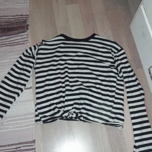 En randig tröja vit och svart - Den är en magtröja med en knut fram.