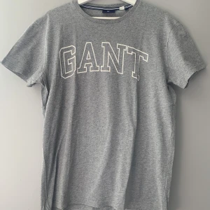 T-shirt  - T-shirt från Gant. Tröjan grå med vit tryck och är i fint skick. 
