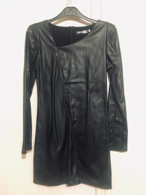 Black pu leather dress - Asymmetrisk urringning, kan bäras med eller utan bälte. Längd axelsöm/fåll 80cm