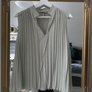 Topp - Söt topp från hm. Plisserad med en ljusgrön/ grå färg. Jättesöt men kommer inte till användning. Som ny. Använd 1 gång 