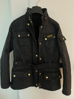 BARBOUR-jacka  - BARBOUR INTERNATIONAL jacka. Storlek: S/M. Strl 36. Quiltad svart med gulddetaljer.  Stålspänne saknas (se bild 5) annars i fint skick.