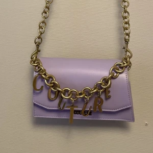 Versace jeans, axelremsväska  - Snygg axelremsväska, från Versace Jeans Couture i fint skick. *Har blivit sparsamt använd, inga skav eller märken. *Ljus lila. *Inköpt för drygt 1 år sen. 
