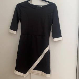 Svart klänning med vita detaljer  - Svart klänning i stretch. Lägger sig fint på benen som inte bilden visar jättebra. Söm i midjan som framhäver figurformen. Använd fåtal gånger 