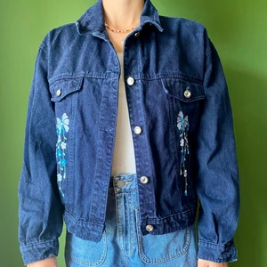 Jeansjacka med blommor  - Jeansjacka i marinblått med blommor på och diamantliknande knappar. Nästan nyskick. 