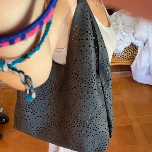 Svart handväska - Har fler bilder som ni ser i bakgrunden på de utzoomade bilderna. Helt oanvänd, köpt i Spanien. Säljer för att jag redan har tillräckligt med väskor. Svart handväska med mönstrade hål som detaljer.