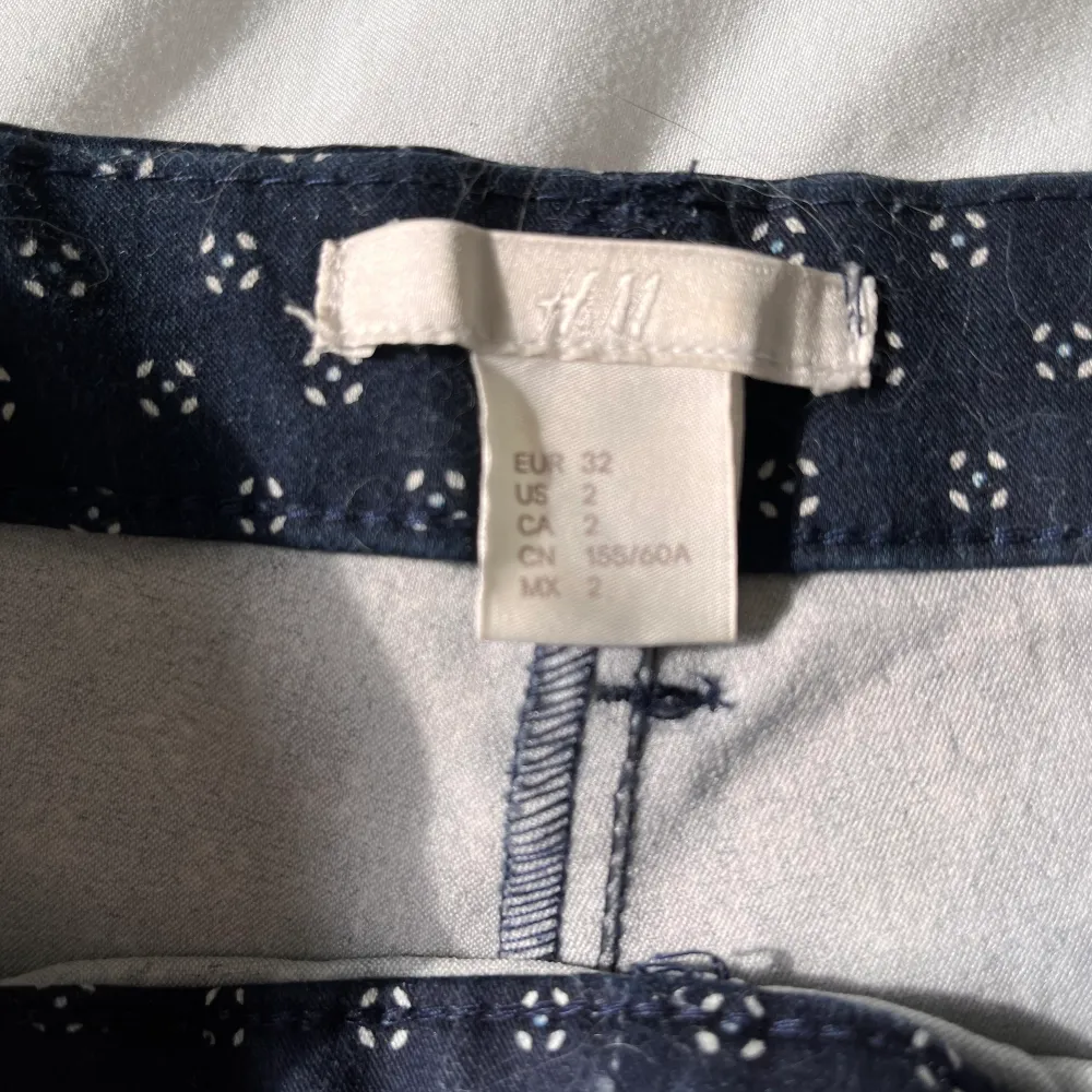 Mörkblå, kostymliknande byxor med vita detaljer på. Strl 32. Ankellängd. Sparsamt använda. Säljes pga för små. . Jeans & Byxor.