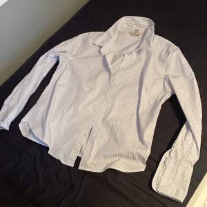 En blå vit randig skjorta från H&M som ej har används alls och är därför i nyskick. Mycket bra passform och ett skönt material, Snygg både stängd och öppen med något under! Orginalpris: 299kr