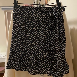 Svart kjol storlek 38 - Supersöt svart kjol med en volang som går upp i en rosett i midjan. Den har resår i midjan vilket gör den väldigt bekväm. Använd någon gång men det är inget som syns.