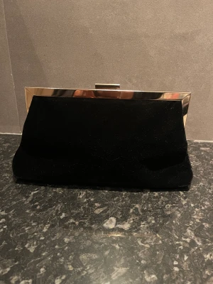 Handväska  - Helt oanvända handväska med tillhörande axelkedja. Guld och svart. 