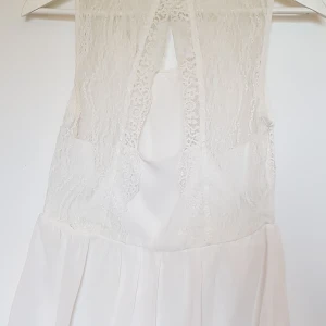 Somrig blus/linne - Vit, somrig blus/linne med öppen rygg och spetsdetaljer med resår i midjan och liten "volang". Använd men inga fläckar. Lappen bortklippt men passar strl S och XS. Tror den kommer från Vila. Pris exkl frakt. Hämtas på Lilla Essingen alt Fridhemsplan.