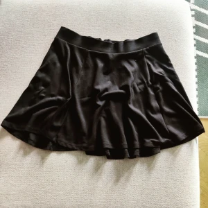 Svart kjol - Svart A line-kjol med volang och dragkedja i guld i bak.