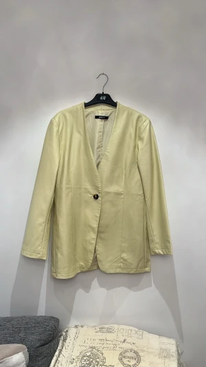 Kavaj  - Enkelknäppt kavaj med en avslappnad passform. Kavajen är ljusgul och har ett fusklädermaterial.