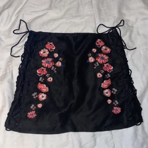 Svart kjol - Svart kjol med blommor och snörning längst benet. Köpt på H&M i Thailand. Storlek 36. Använd några gånger en sommar.