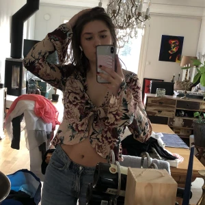 Blommig topp - SUPERSÖT blommig knytbar top! Perfekt nu till i vår och sommar, den är i siden material och är super skön, från Gina. Storlek S.