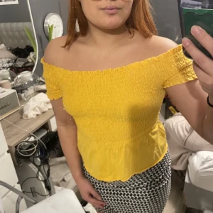 Gul smockad tröja - Gul t-shirt med volang från Gina Tricot. Storlek S men passar både större och mindre pga smockningen. Finns i svart också.