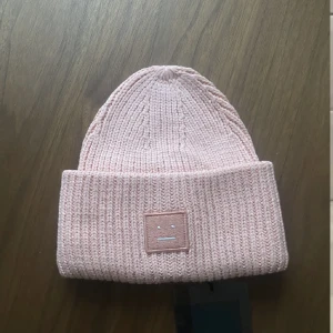 BEANIE ACNE - Oanvänd mössa från Acne i ljus korall. Frakt tillkommer på 49 kr. 