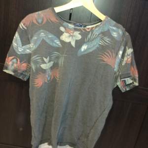 En grå t-shirt med tropisk mönster. Den är i fint skick och köparen står för frakten:)