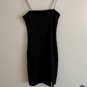 Svart tight klänning  - Kort klänning som har en liten slitts nere vid låret, den har silvriga diamant axelband.