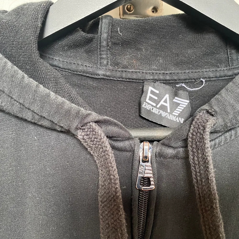 Säljer min EA7 kofta, den är svart med silver text, det enda problemet med den är att märket sitter lite löst vid nacken som ni kan se. Ganska liten storlek. . Tröjor & Koftor.