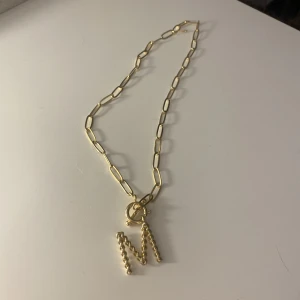 Halsband med M - Ett halsband där det står ett M på. Aldrig använt 