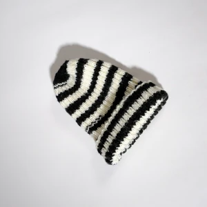 Stickad svartvit mössa  - One-of-a-kind stickad svartvit mössa. Stickad av Röda Korsets-stickgrupp i Västerort tillsammans med Ebba Martin. Alla pengar från budgivningen går oavkortat till Röda Korsets arbete för att hjälpa människor i kris och katastrofer.