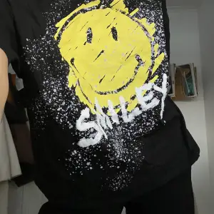 En svart T-shirt med smiley-tryck! Oversized i storlek S men hade passat M i både herr och dam. Helt oanvänd😋