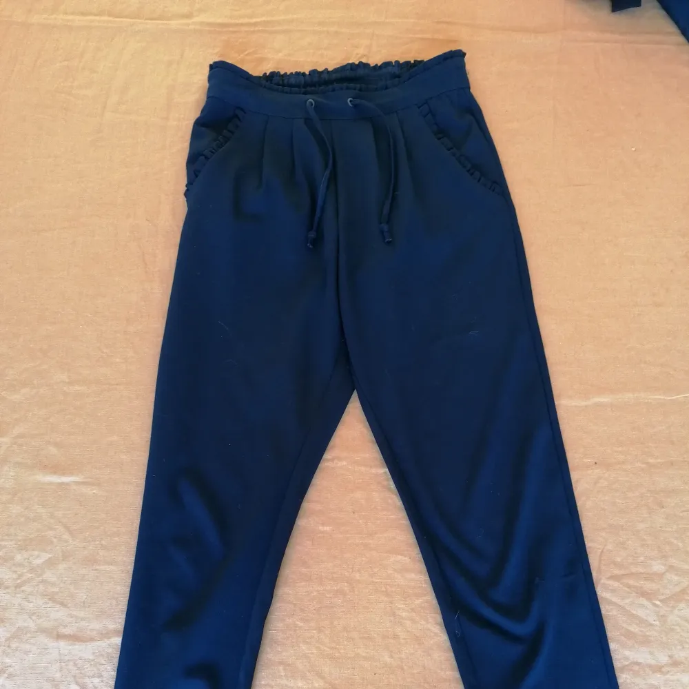 Slack/kostymbyxa i polyester material. Marinblå och från Jacqueline de Yong. Små volanger i fickor och midja. . Jeans & Byxor.