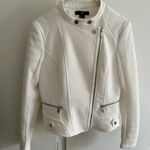 Vit jacka strl 38 - En vit tunn jacka ifrån H&M i strl 38. Liknar lite en skinnjacka i modellen men är i tyg, säljes pga används ej. Hör av dig för mer info! 