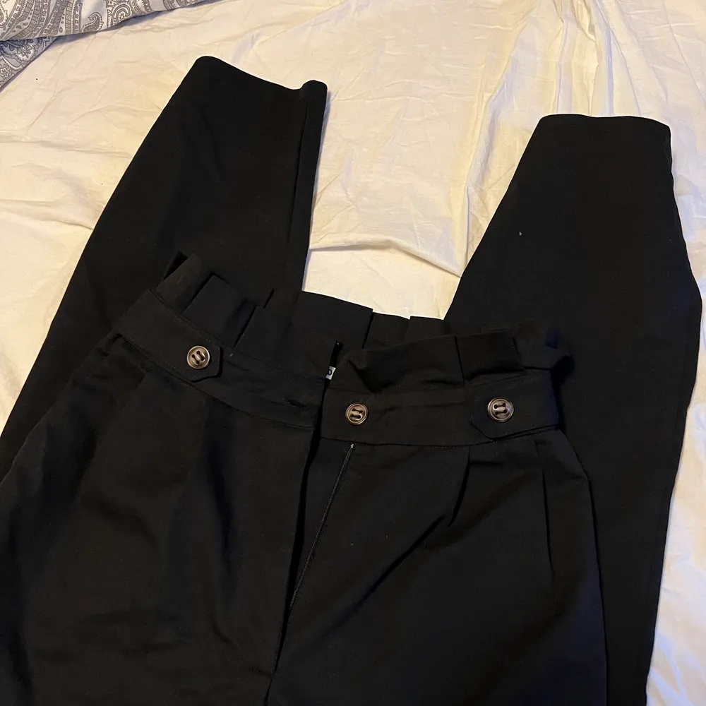 Svarta kostymbyxor från NA-KD med snygga knappar på sidor. Storlek 34. Använd enstaka gånger.. Jeans & Byxor.