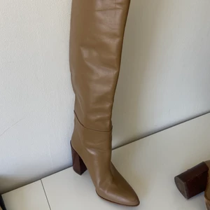Höga stövlar  - Höga stövlar i Beige från Zara. Knähöga, modellen är lite skrynklad över vaden, klackhöjd 10 cm. Lite små skada längst fram vid tippen, använda två gånger. Passar för mig som har stl 37-38.
