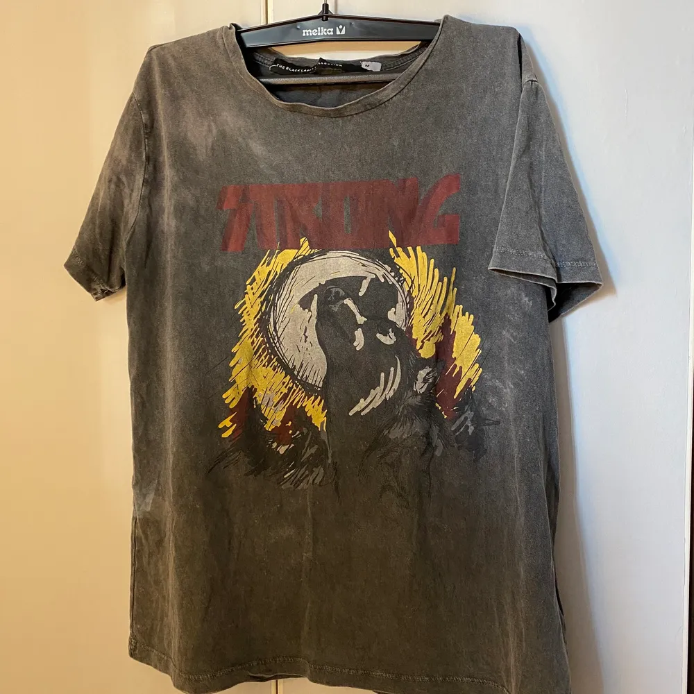 En grå tshirt med tryck från lager 157. På trycket är det en hund/ varg, en måne och texten ”strong” ovanför i rött.. T-shirts.