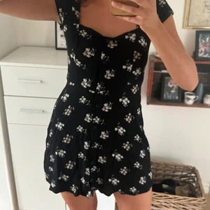 Svart klänning från hollister - Svart kort klänning med vita blommor på med knappar längst framsidan. Storlek medium. Dragkedja längst vänstra sidan.