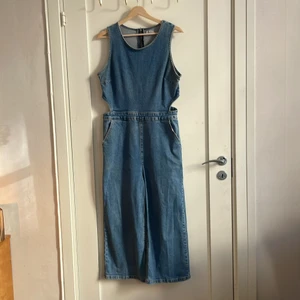 Jeans-jumpsuit i storlek 44 - Jumpsuit i jeans med cut out design mot revbenen. I storlek 44 från brittiska New Look. Sparsamt använd. 