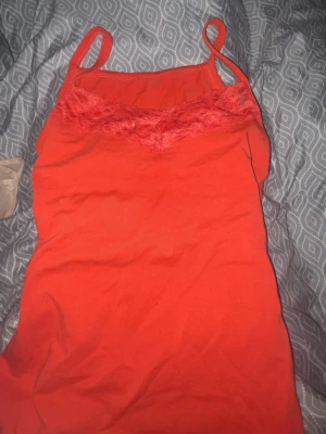 Röd linnetopp med spetskant - Snygg röd linnetopp med tunna axelband och dekorativ spetskant vid urringningen. Perfekt för att addera lite färg till din outfit. Tillverkad i mjukt material som känns skönt mot huden.