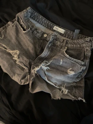 Grå/svarta slitna jeansshorts från Zara - Säljer ett par grå/svarta jeansshorts från Zara med råa kanter och slitna detaljer. Shortsen har dragkedja framtill. Perfekta för en avslappnad look under varma dagar❤️