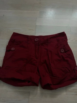Mörkröda shorts med fickor och knappar H&M - Snygga mörkröda shorts med uppvikta ben, flera fickor med knappstängning och knapp i midjan. Perfekta för varma dagar och har en avslappnad passform. Tillverkade i bomull för skön känsla.