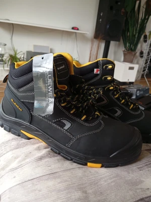 Svarta skyddsskor från Bluewear - Säljer ett par svarta kängor från Bluewear med gula detaljer och snörning. Kängorna har robust sula, förstärkt tå och kontrastsömmar. Insidan är fodrad med gult tyg och skorna har metallhål för snören. Perfekta för dig som vill ha slitstarka och snygga kängor.