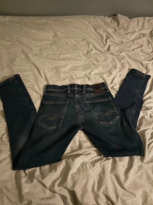 Mörkblå slim fit jeans med kontrastsömmar - Säljer ett par mörkblå slim fit jeans med snygga kontrastsömmar på bakfickorna och klassisk femficksdesign. Jeansen har en läderpatch vid linningen och är tillverkade i ett stretchigt denimtyg för skön passform. Hör av er vid frågor och funderingar😃