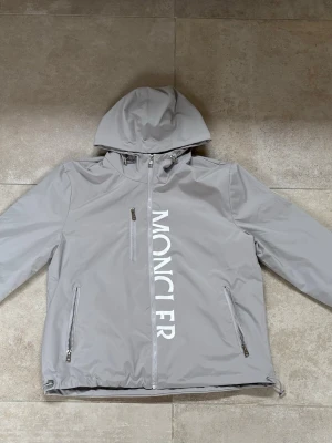Ljusgrå vindjacka från Moncler - Helt ny moncler windbreaker använd bara en gång pga fel storlek inga fel och inga problem med jackan. Priset kan sänkas genom snabb affär.