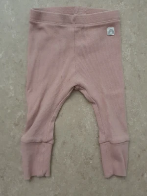 Leggings - Supersöta ljusrosa leggings i ribbad bomull med breda muddar och uppvik vid bensluten. Liten tygpatch med regnbåge framtill. Perfekta för en chill och bekväm stil.